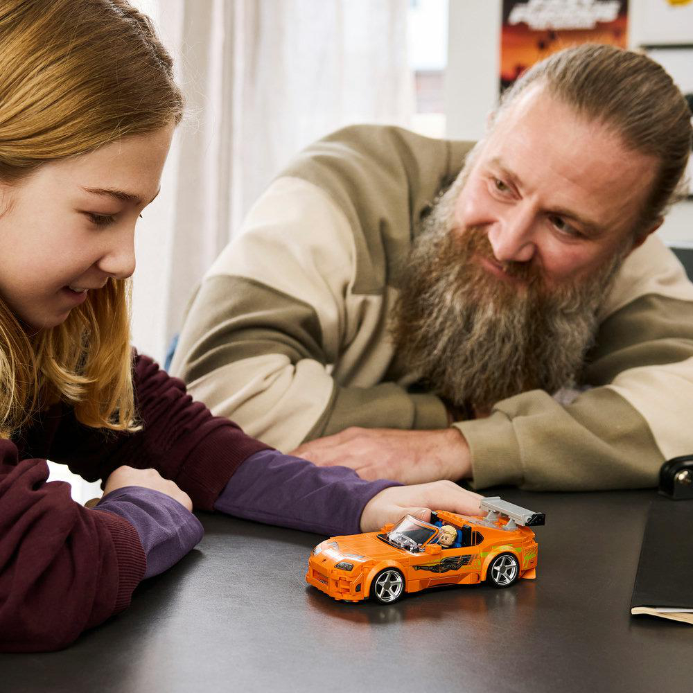 Ein Mann mit Bart und ein Mädchen schauen auf ein orangefarbenes Spielzeugauto.