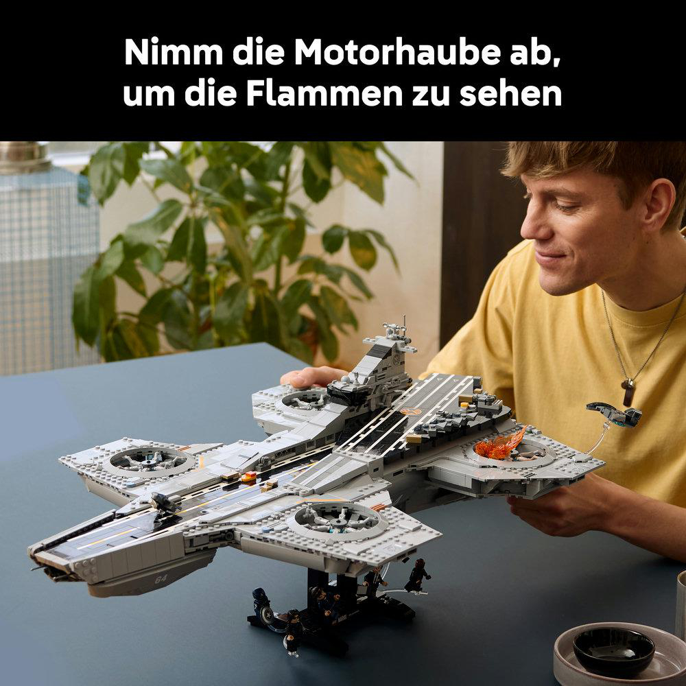 Mann mit gelbem Hemd baut graues Lego-Raumschiff mit Flammen-Detail.