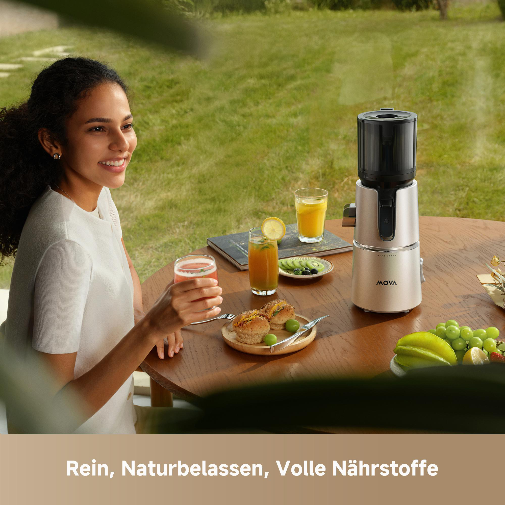 Frau trinkt Saft am Tisch mit Entsafter, Gebäck und Obst im Freien.