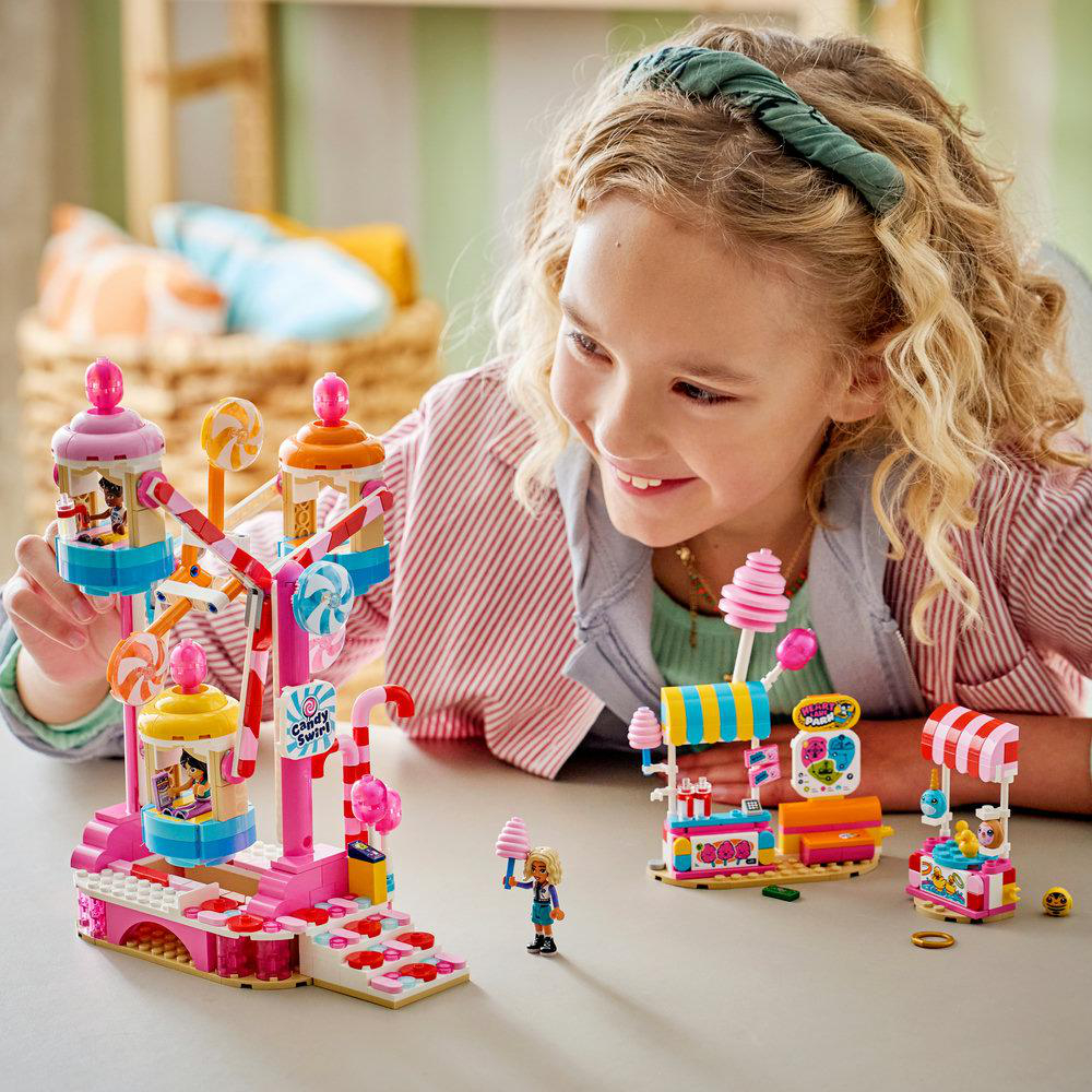Mädchen spielt mit bunten Lego-Vergnügungspark-Sets zum Thema Süßigkeiten, darunter ein Riesenrad und Stände.