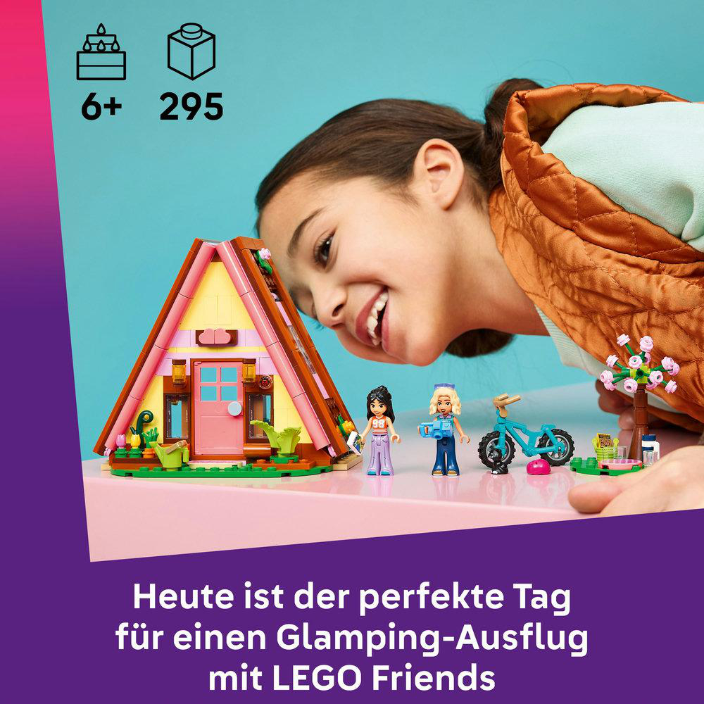Mädchen lächelt, baut eine pinke A-Frame-Hütte mit LEGO Friends Figuren, Fahrrad und Baum.