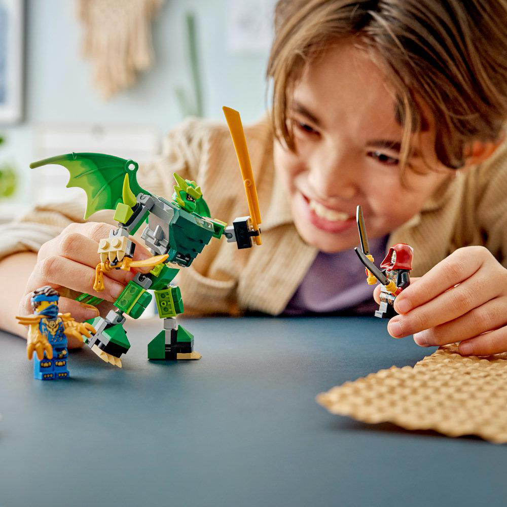 Junge spielt mit grünem Lego-Drachenroboter, blauen und roten Lego-Figuren und Schwertern.
