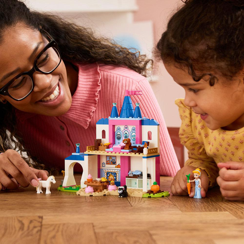 Mutter und Kind bauen eine rosafarbene Burg mit blauen Türmen und Spielfiguren.