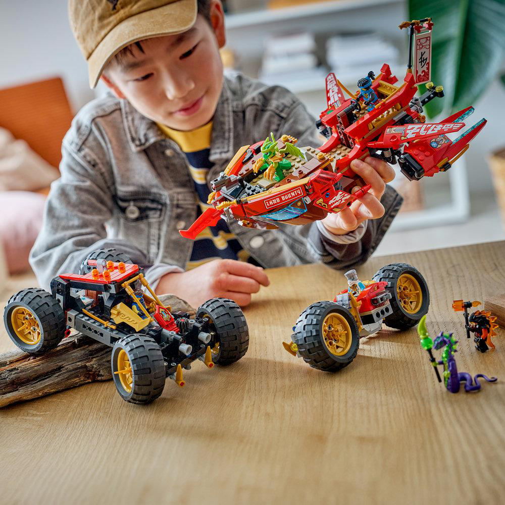 Ein Junge spielt mit roten und gelben Lego-Fahrzeugen und Figuren auf einem Holztisch.