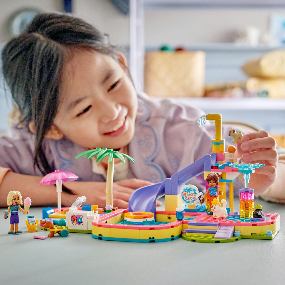 Ein Mädchen spielt mit einem bunten Lego-Wasserpark mit Rutschen und Figuren.