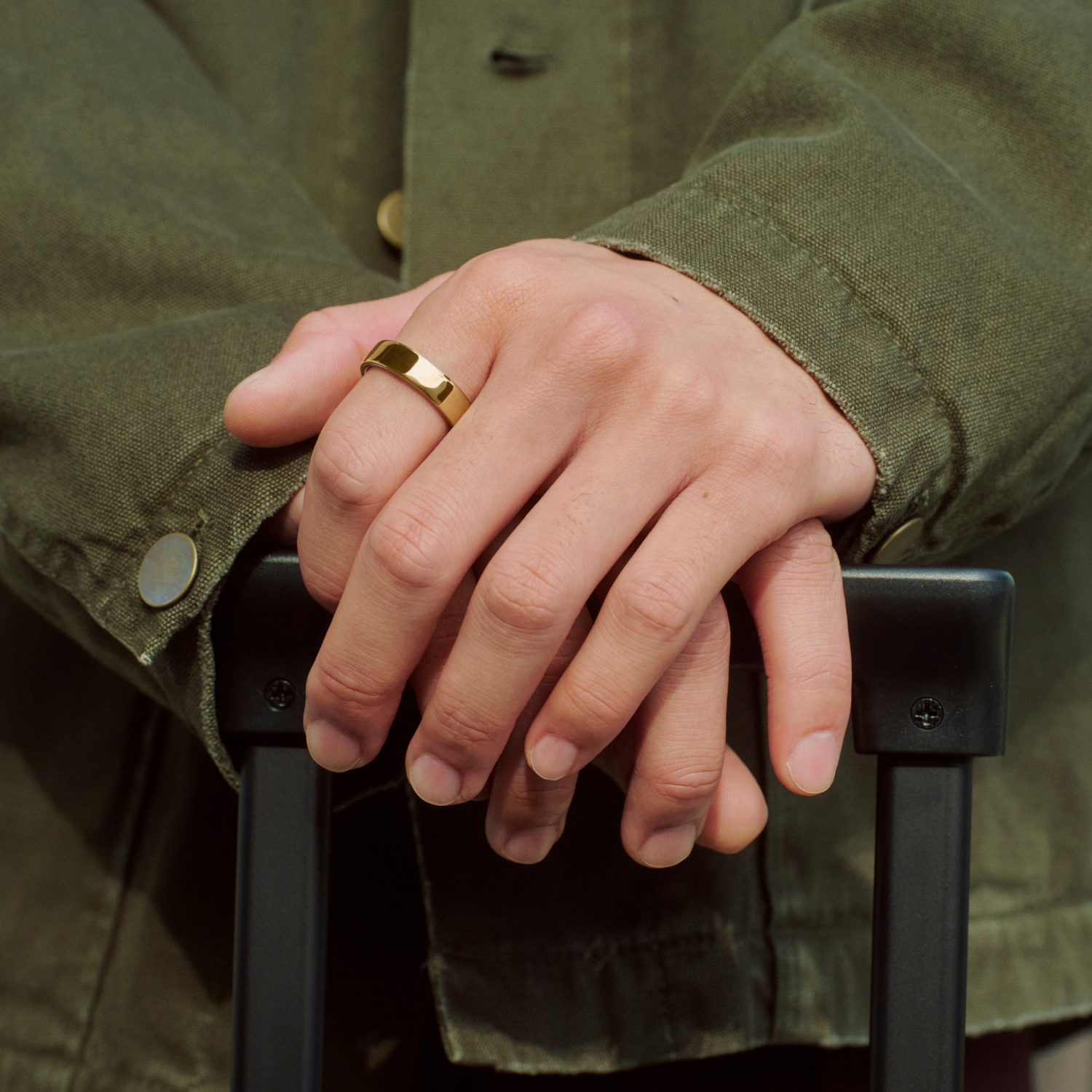 Manos con anillo de oro en asa negra, chaqueta verde