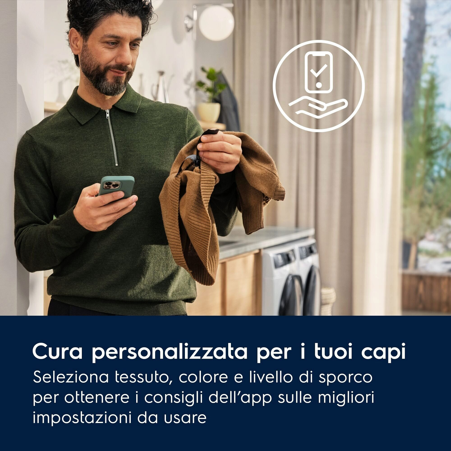 Uomo con smartphone e maglione marrone davanti a lavatrice e finestra.