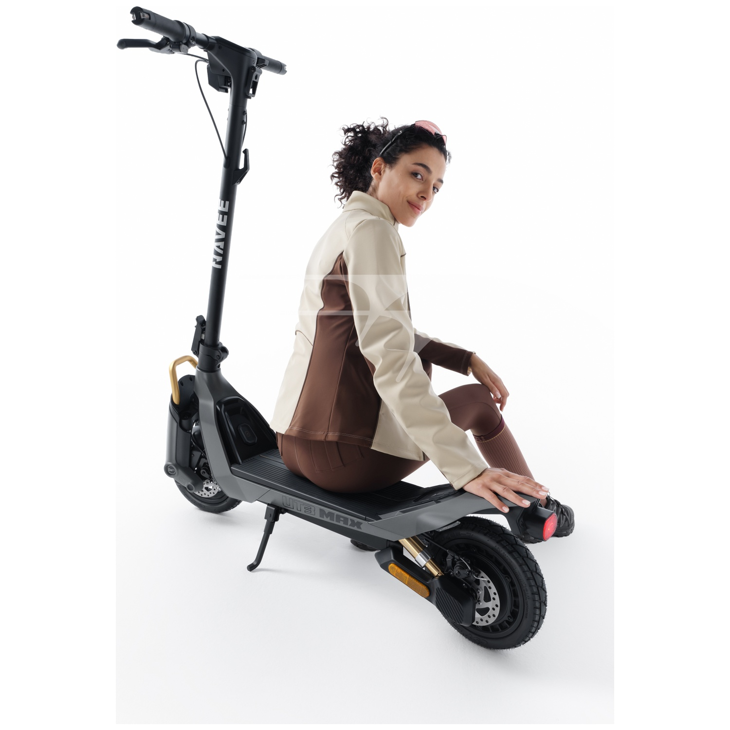 A woman in a beige and brown jacket sits on a gray electric scooter.