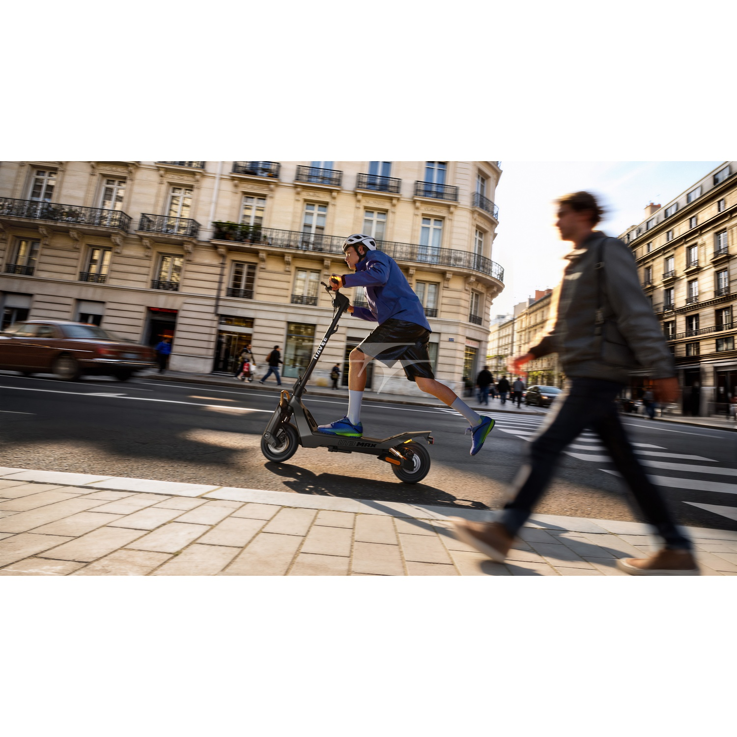 A man rides an electric scooter on a Paris street as another man walks by.