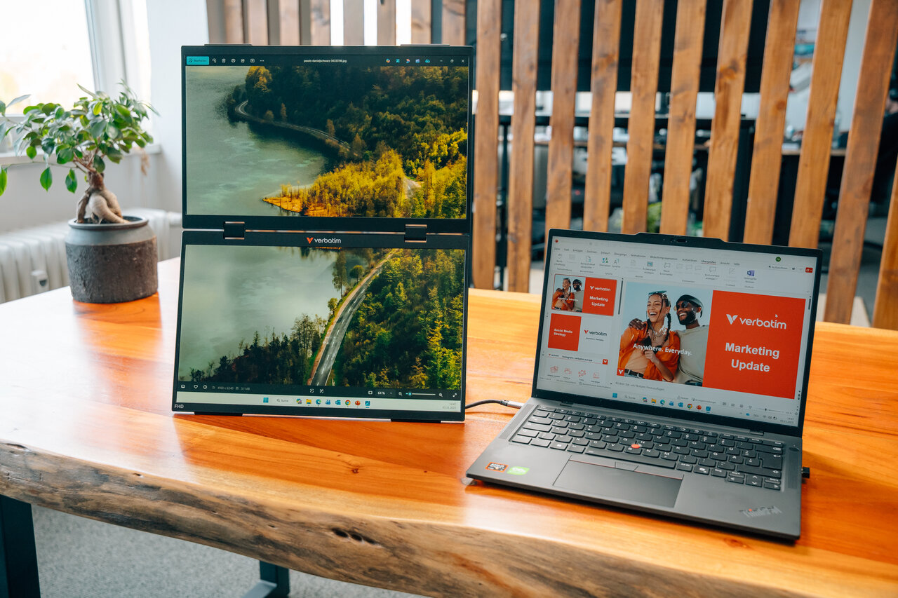 Ein Laptop und ein vertikaler Monitor stehen auf einem Holztisch. Beide zeigen eine Landschaft.