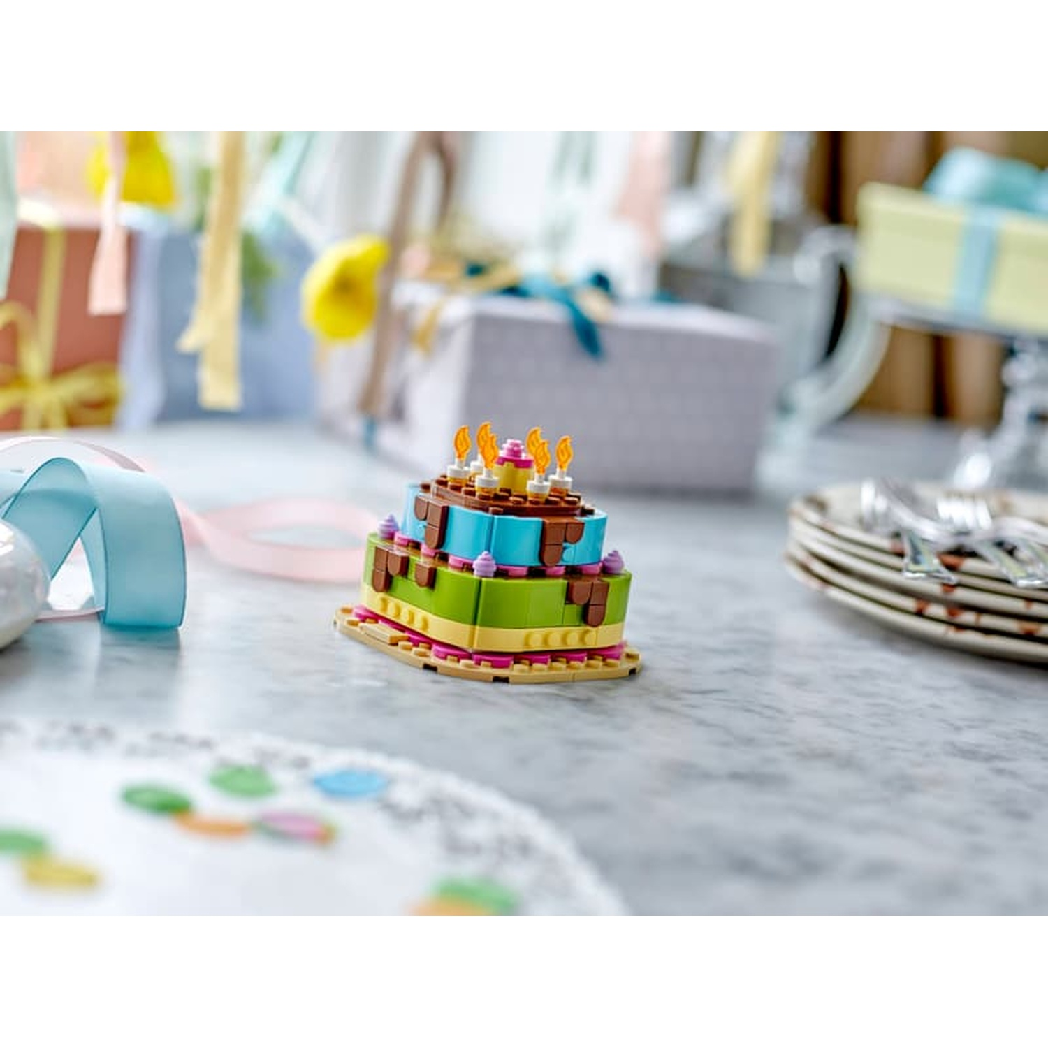 Un gâteau d'anniversaire Lego à plusieurs étages avec des bougies sur une surface en marbre.
