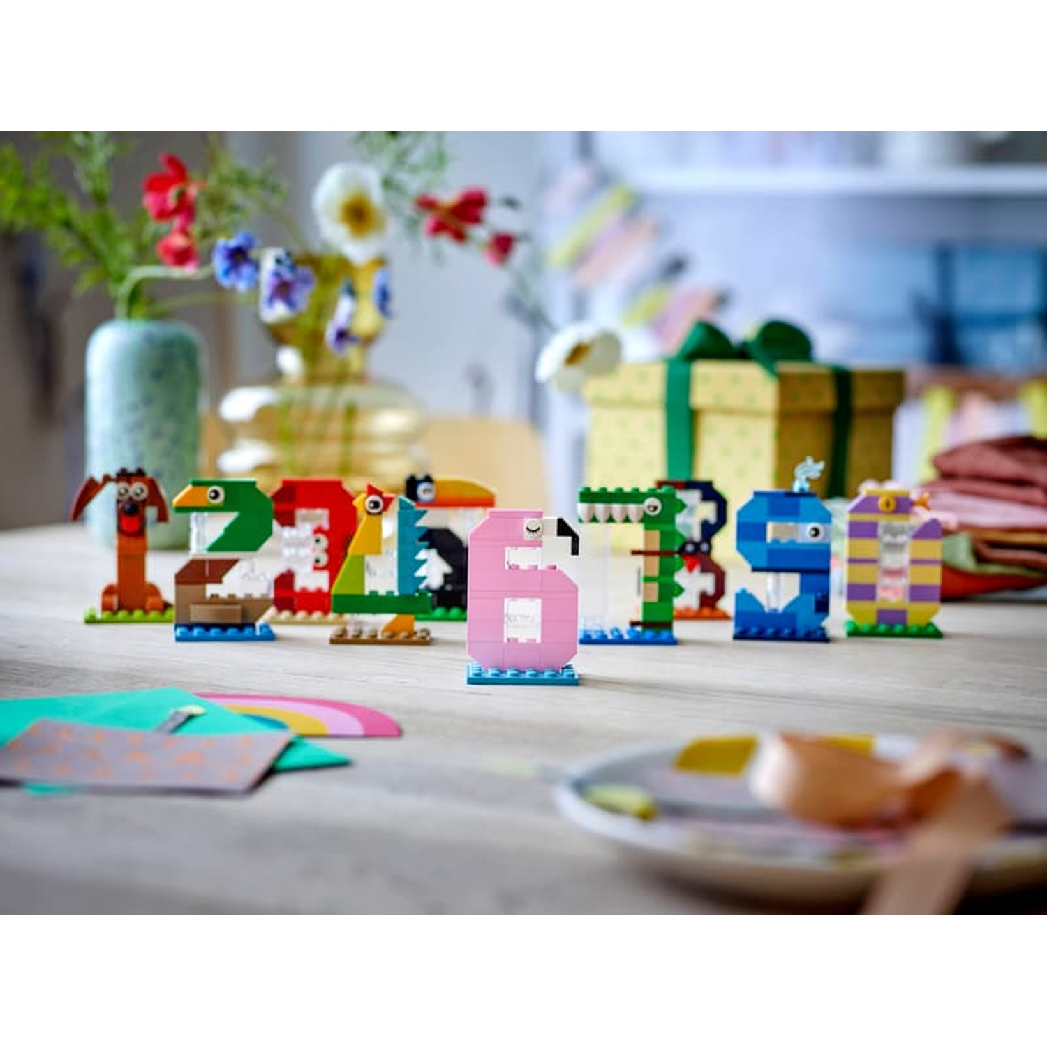 Chiffres Lego colorés 1-9 en animaux sur une table en bois avec fleurs et cadeaux.
