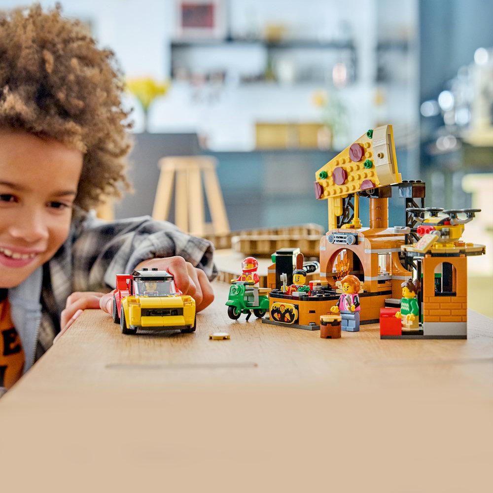 Ein Junge spielt mit einem Lego-Pizza-Laden-Set, inklusive Auto, Roller und Figuren.
