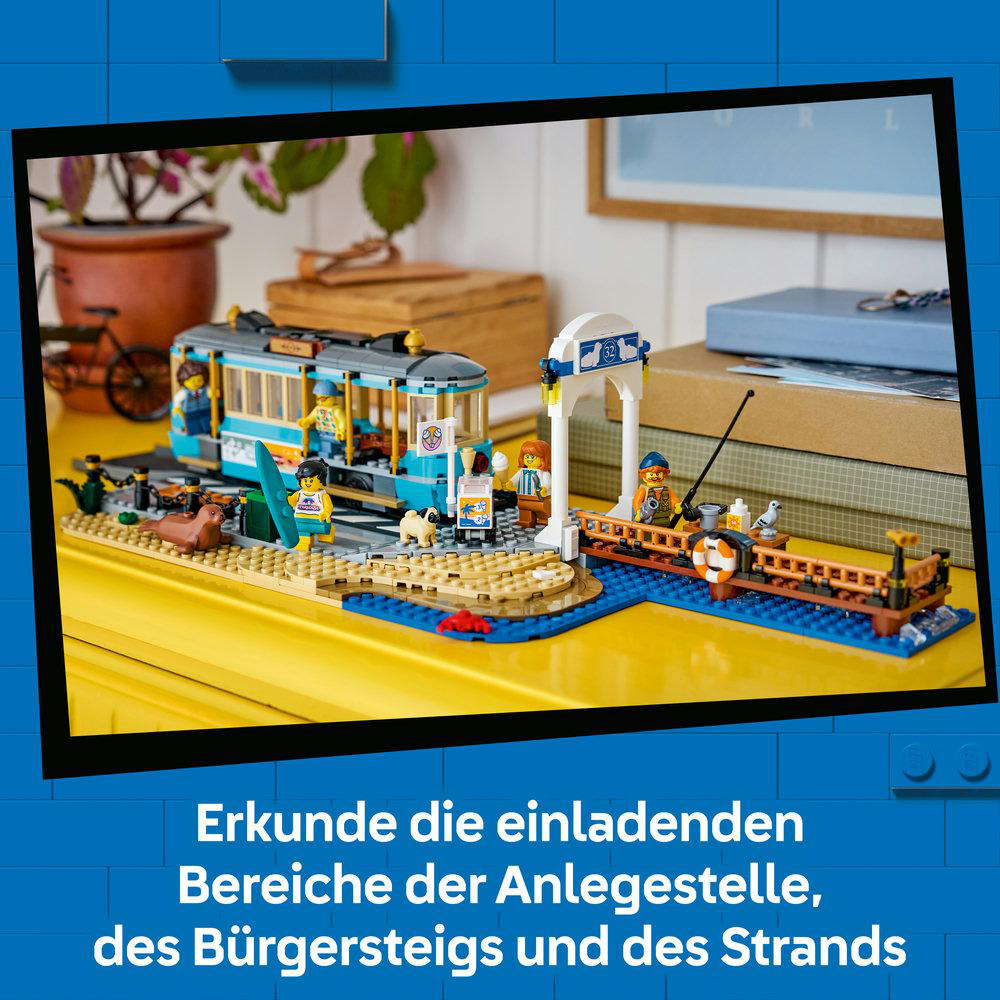 Lego-Set mit Tram, Pier und Strandfiguren. Ein Tram fährt auf Gleisen, neben einem Steg mit Angler.