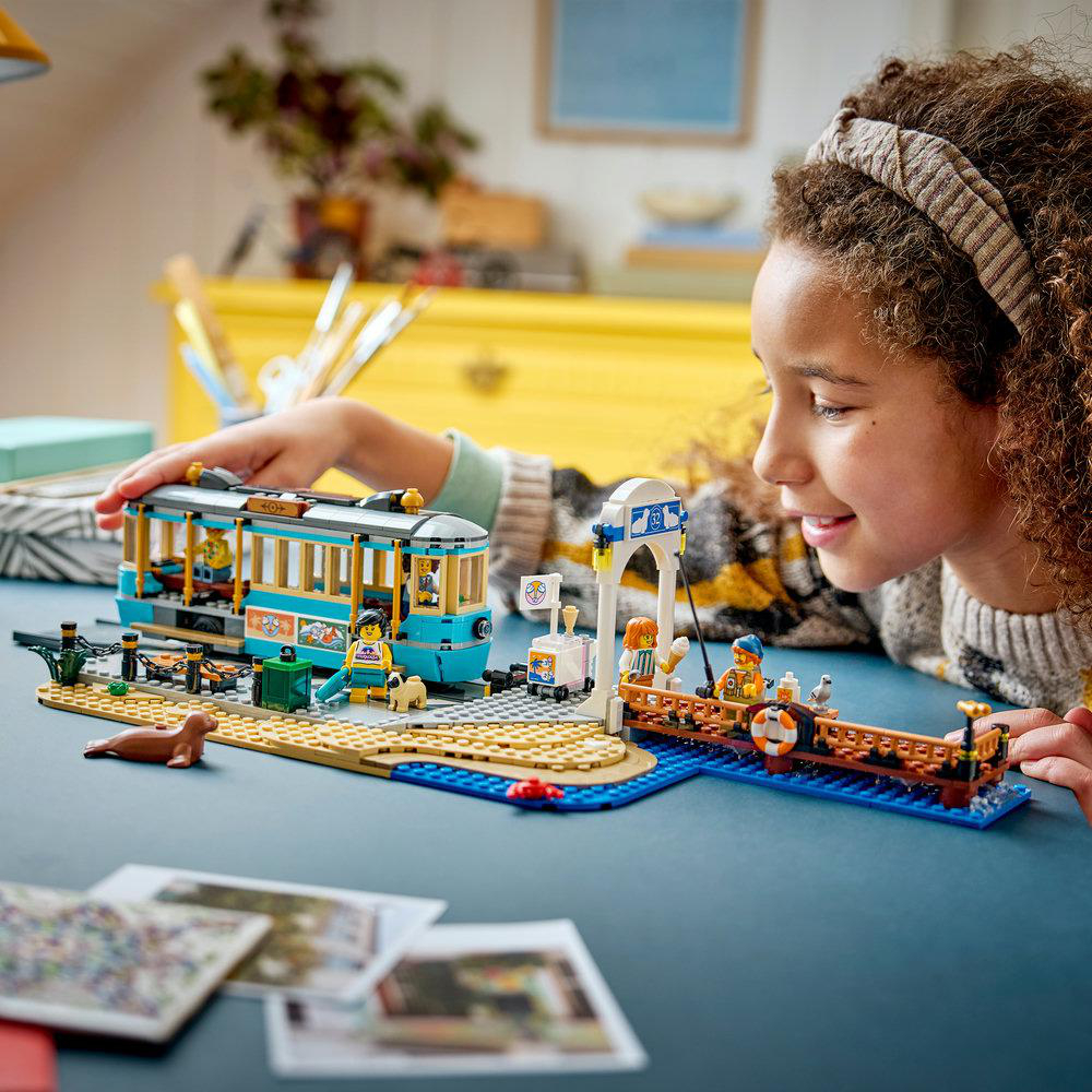 Ein Kind spielt mit einem Lego-Straßenbahn- und Pier-Set mit Figuren, einer Robbe und einem Boot.