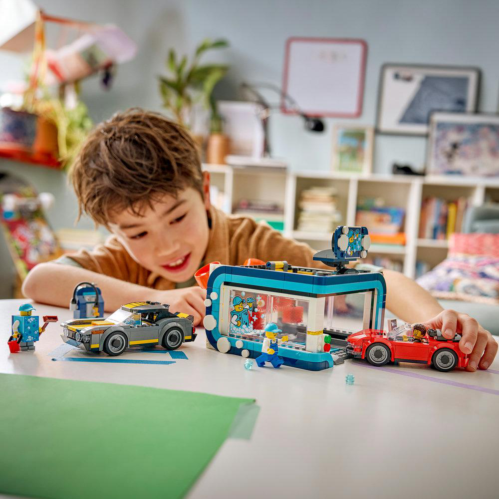 Junge spielt mit Lego-Autos und einer Waschanlage auf einem Tisch.