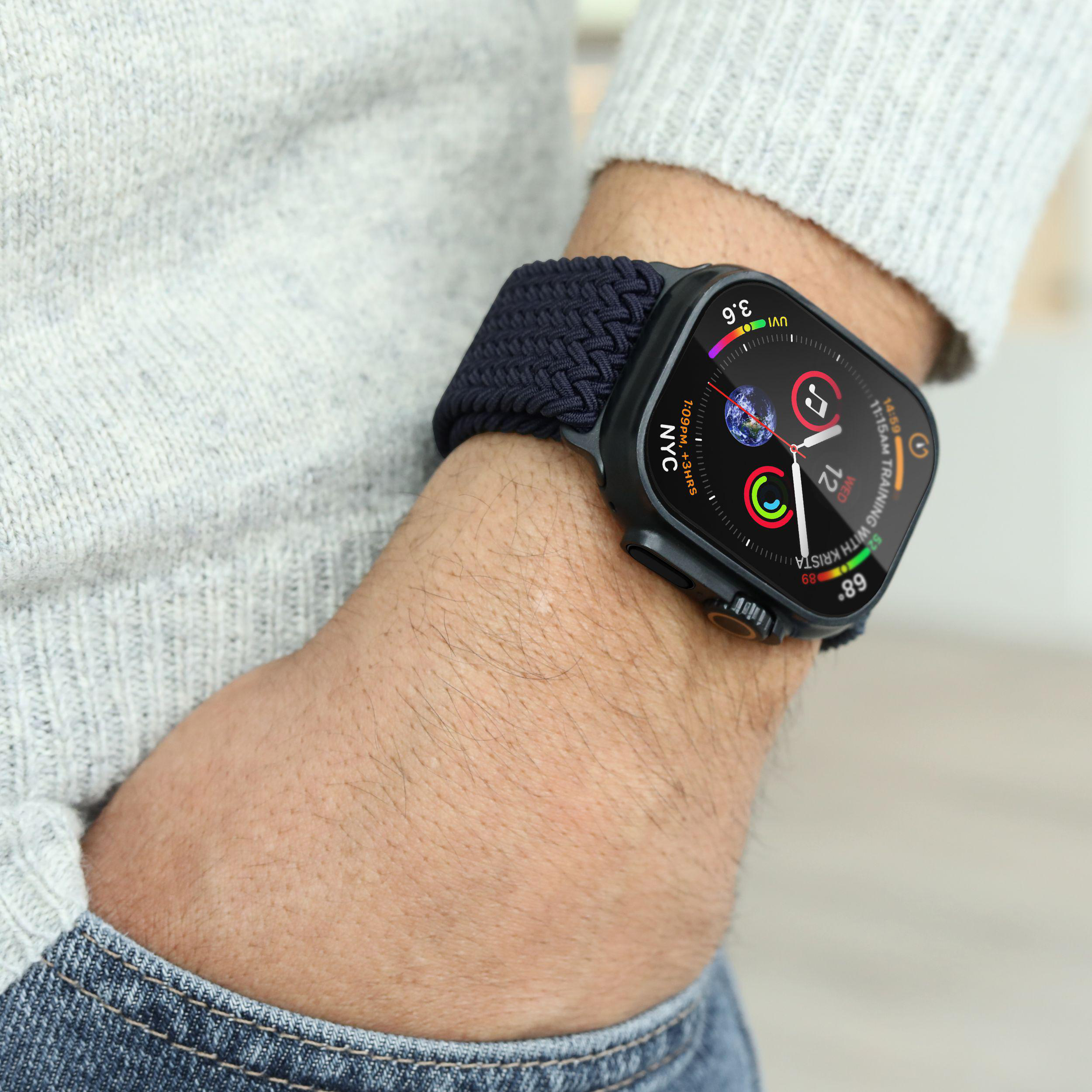 Eine Person trägt eine dunkle Smartwatch mit blauem Stoffarmband. Die Uhr zeigt 12, Mittwoch und 89 Grad.