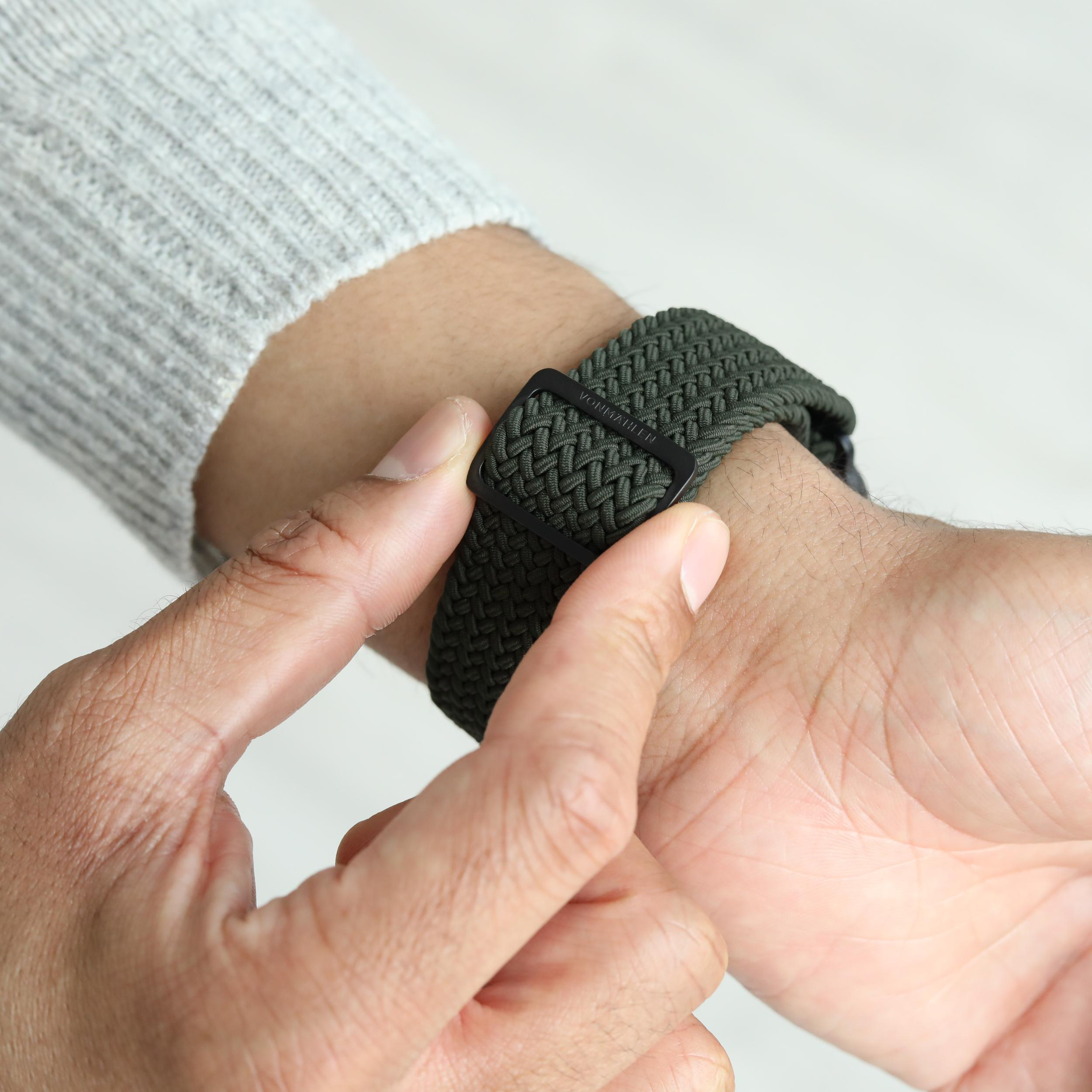 Grünes Armband mit schwarzem Verschluss, das an einem Handgelenk befestigt wird.