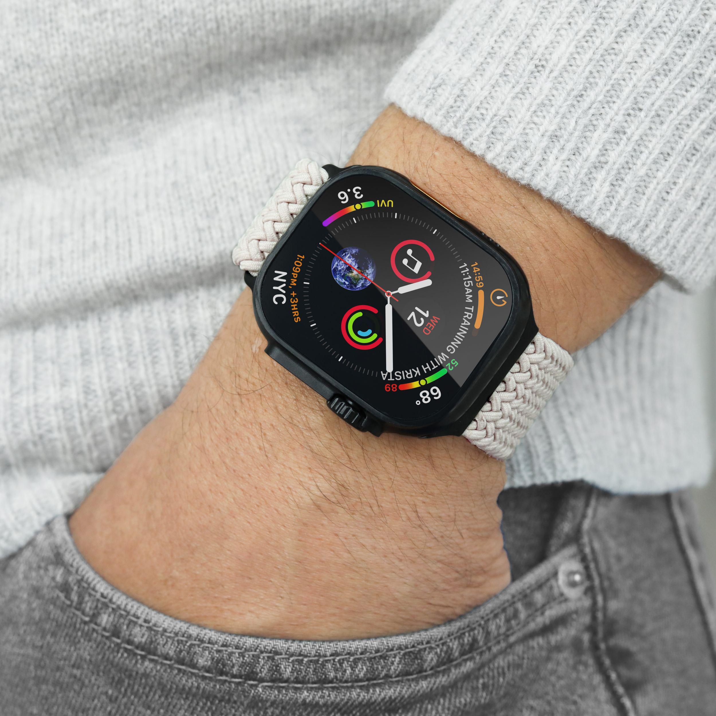 Eine Person trägt eine Smartwatch mit einem geflochtenen Band über einem grauen Pullover und Jeans.