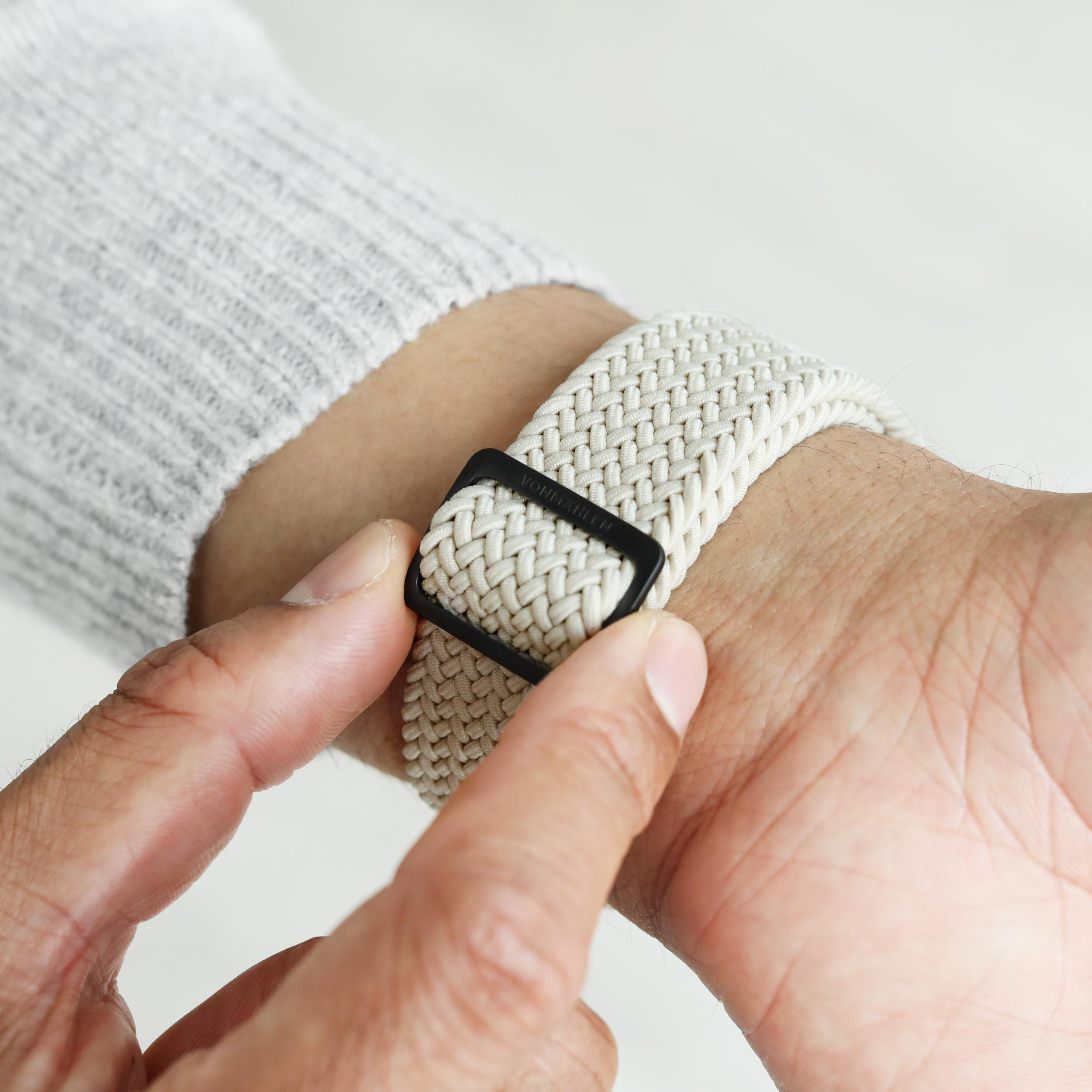 Ein Mann passt ein hellbeiges, gewebtes Armband mit schwarzer Schnalle an sein Handgelenk an.