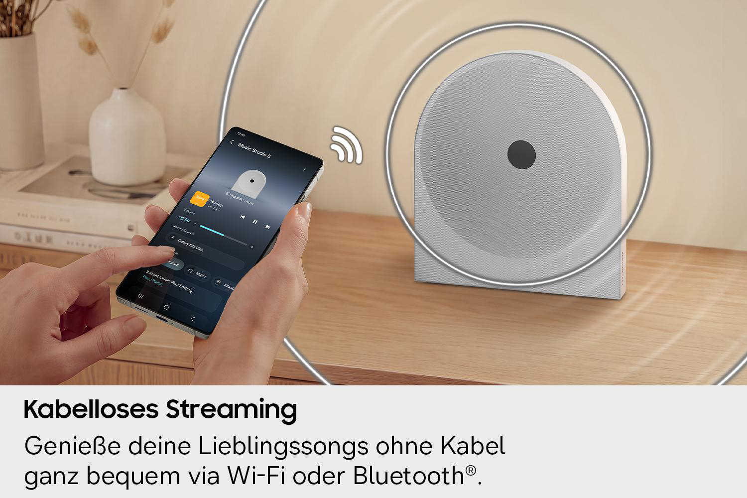 Eine Hand hält ein Smartphone, das eine Musik-App anzeigt, neben einem weißen Lautsprecher.