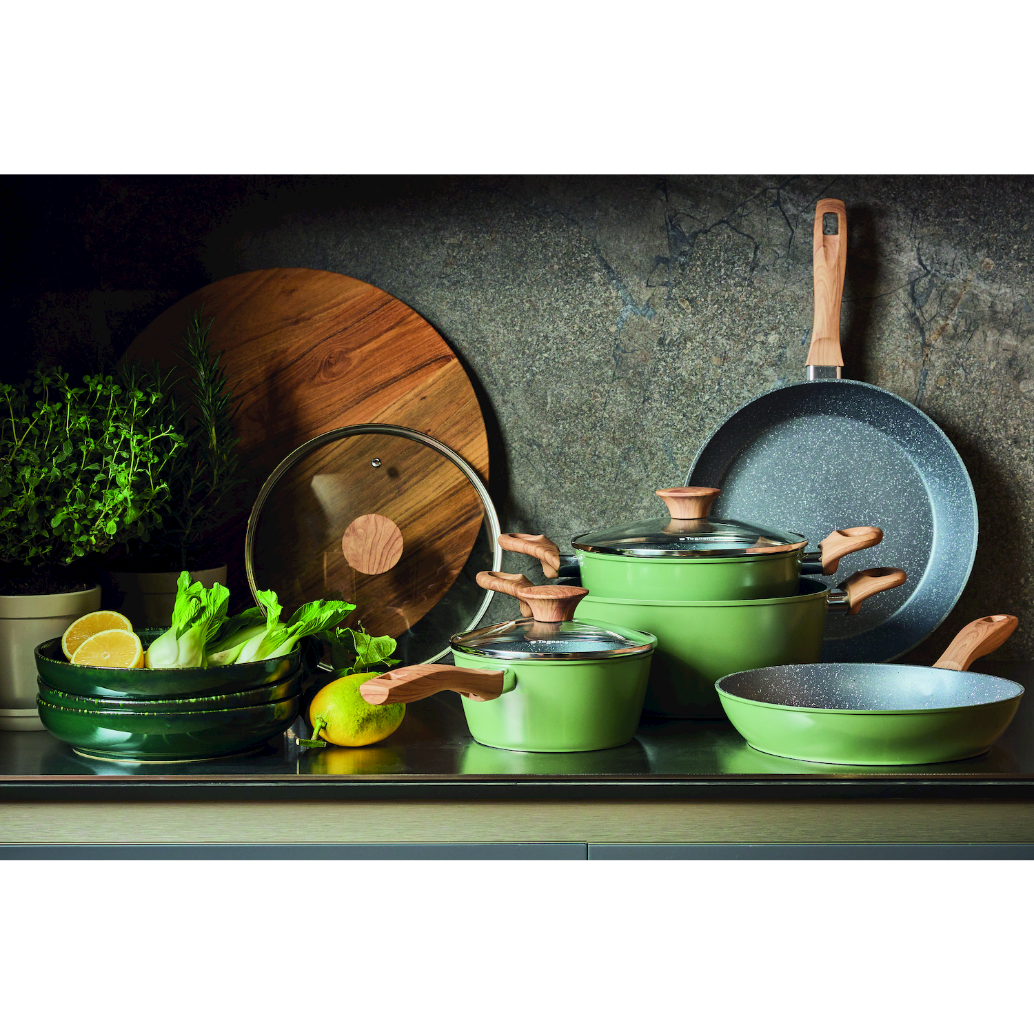 Set di pentole verdi con manici in legno, limoni, verdure e tagliere in legno.