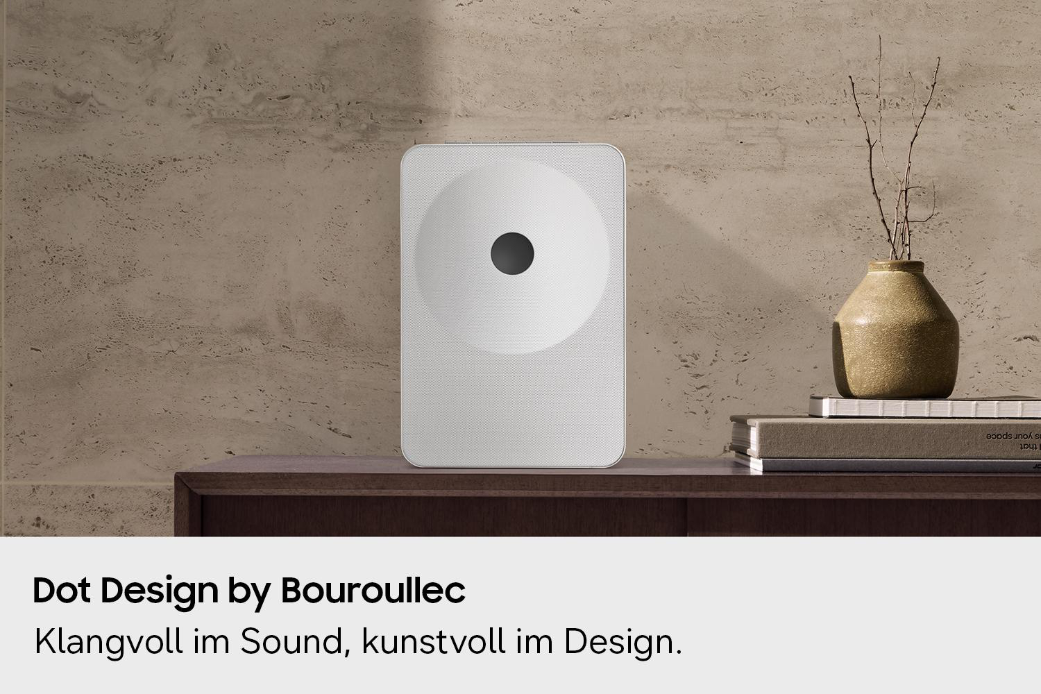 Ein weißer Lautsprecher steht auf einem Regal neben einer Vase und Büchern.