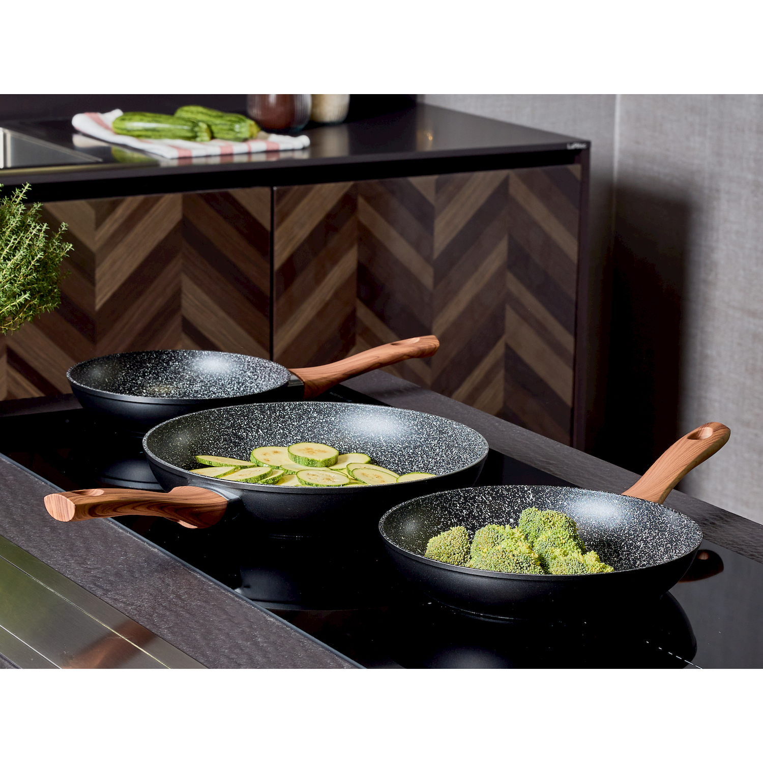 Tre padelle con manici in legno su un piano cottura a induzione, riempite con broccoli e zucchine.