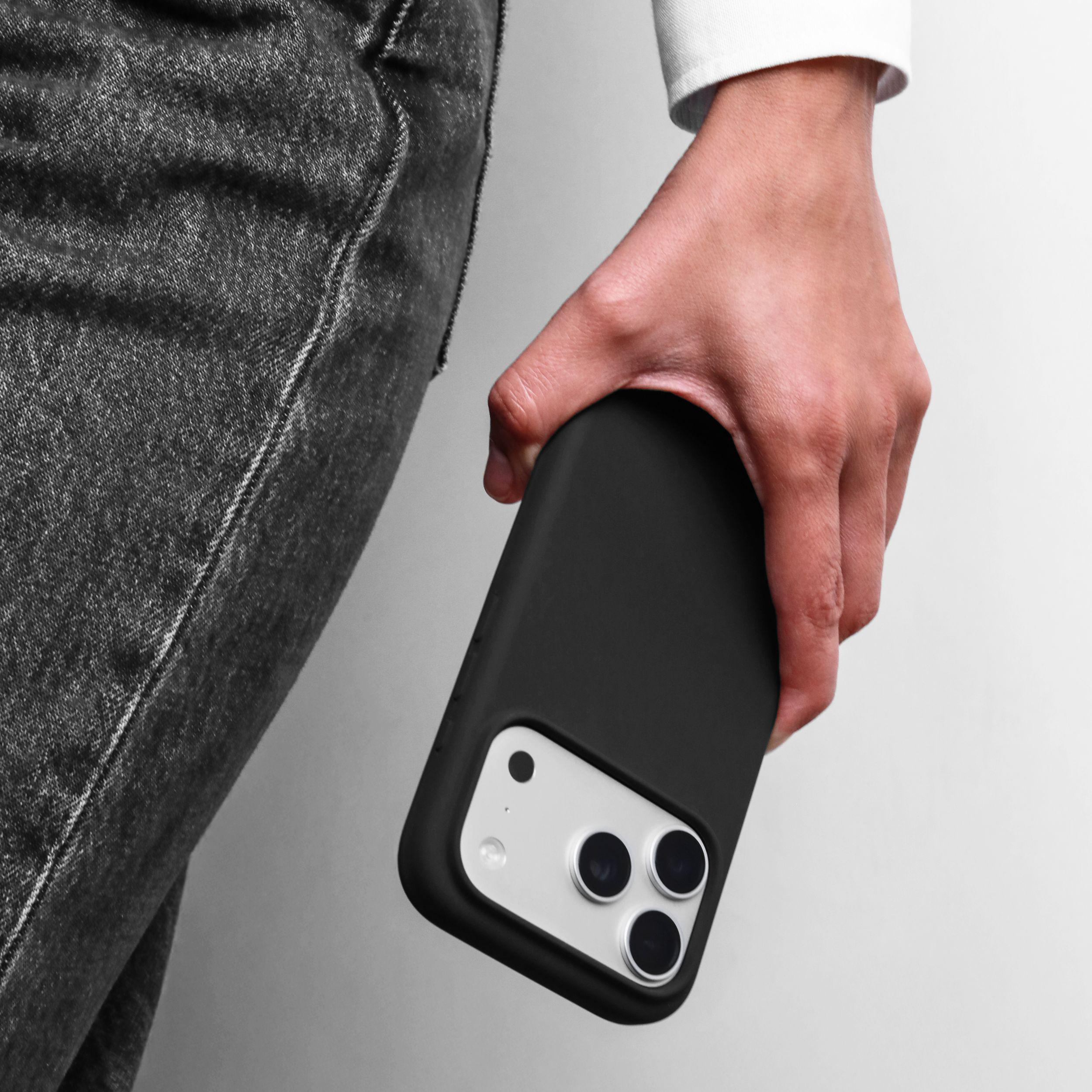 Eine Hand hält ein schwarzes Smartphone mit drei Kameras vor einem grauen Hintergrund.