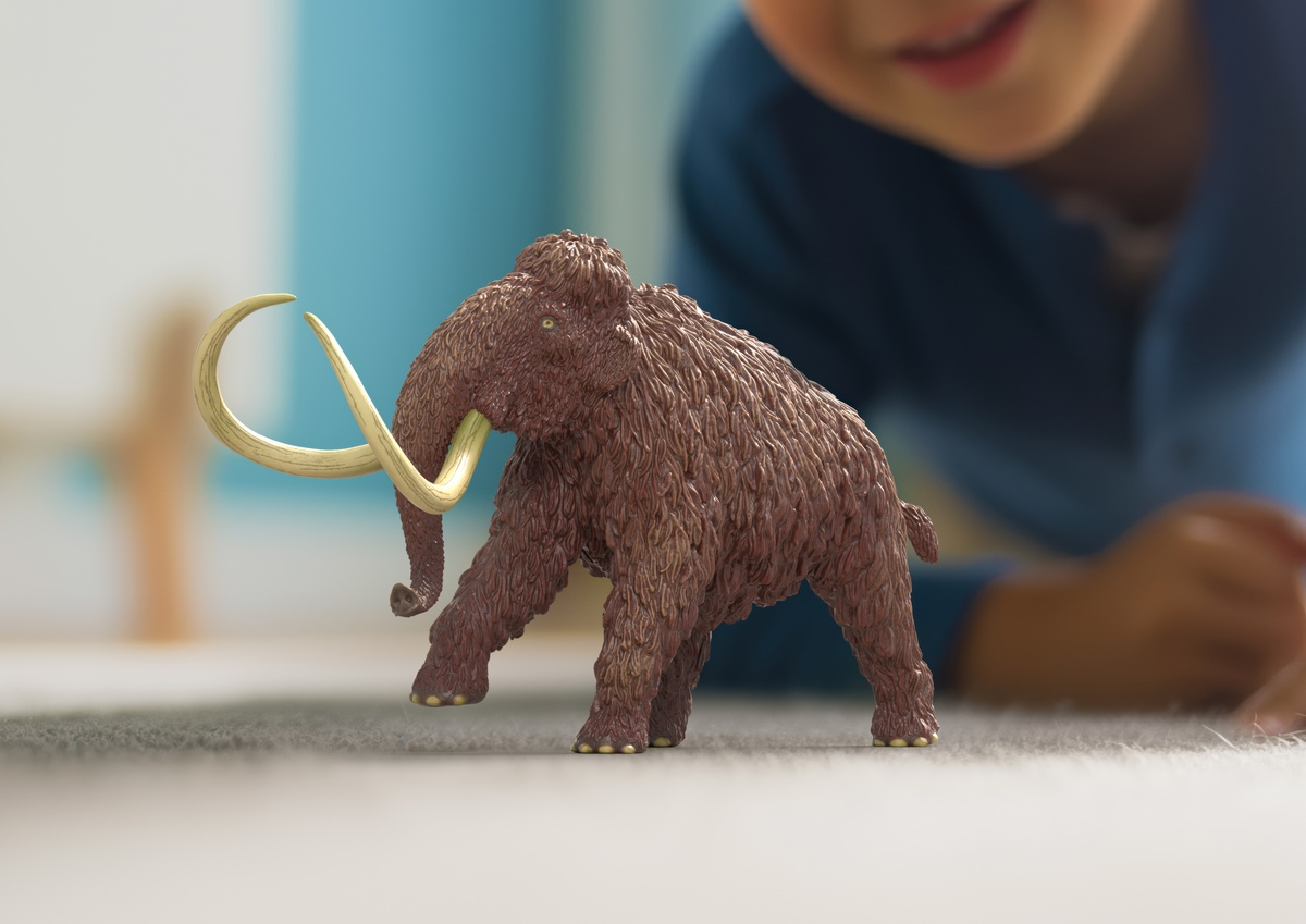 Ein Spielzeugmammut mit Stoßzähnen liegt auf einem Teppich, ein Kind spielt im Hintergrund.