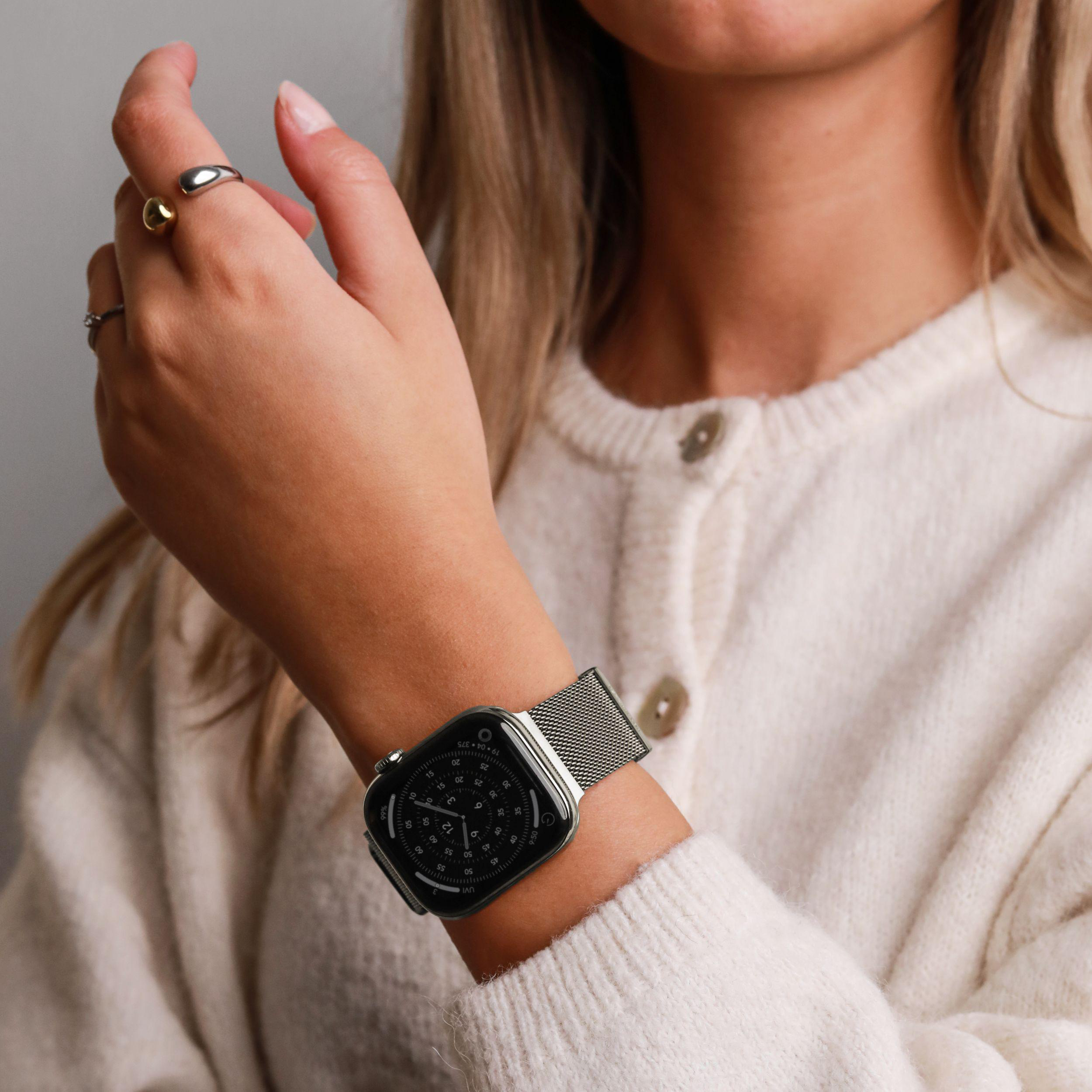 Eine Frau mit blonden Haaren trägt einen cremefarbenen Pullover und eine Smartwatch.