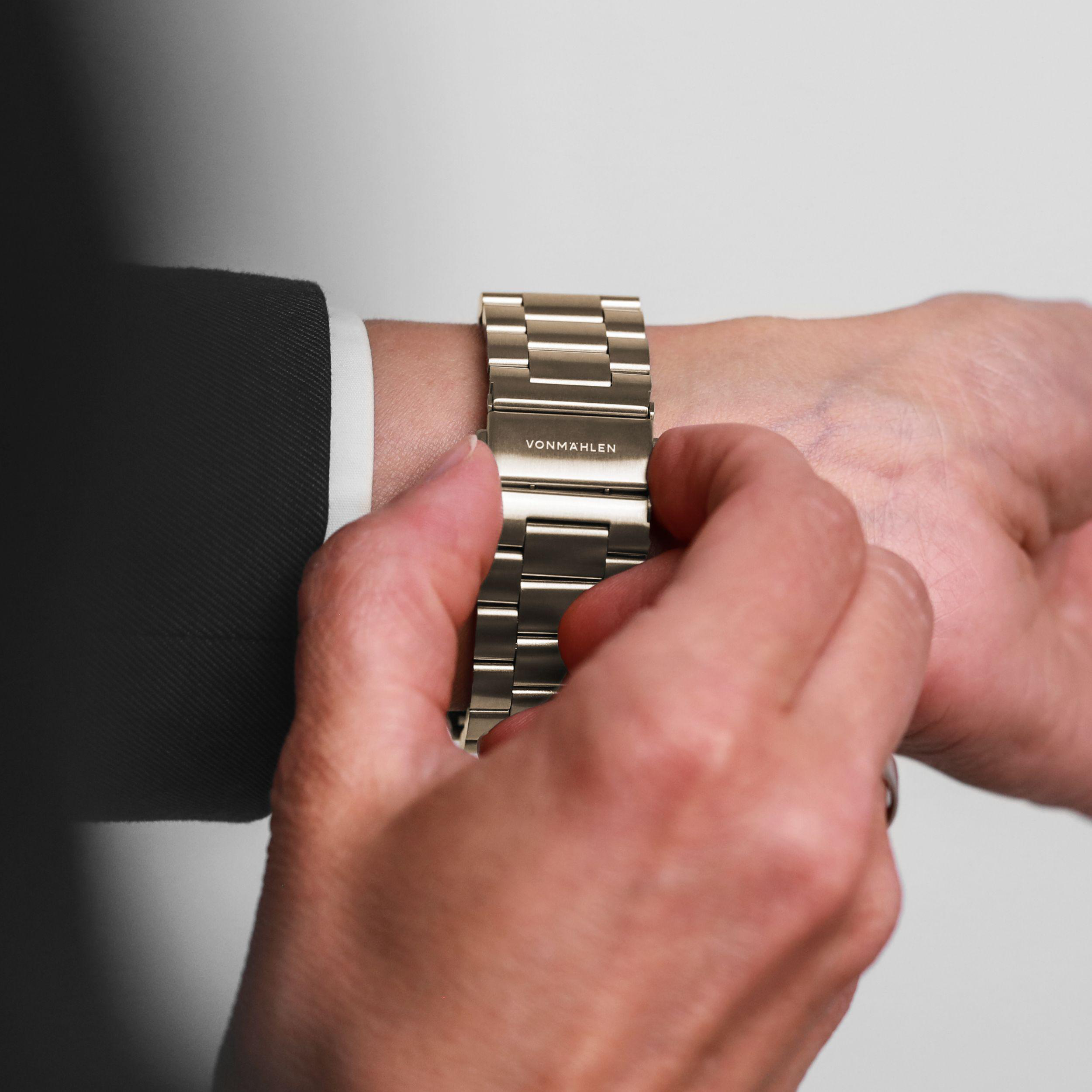 Eine Person in einem dunklen Anzug stellt eine silberne Uhr am Handgelenk ein.