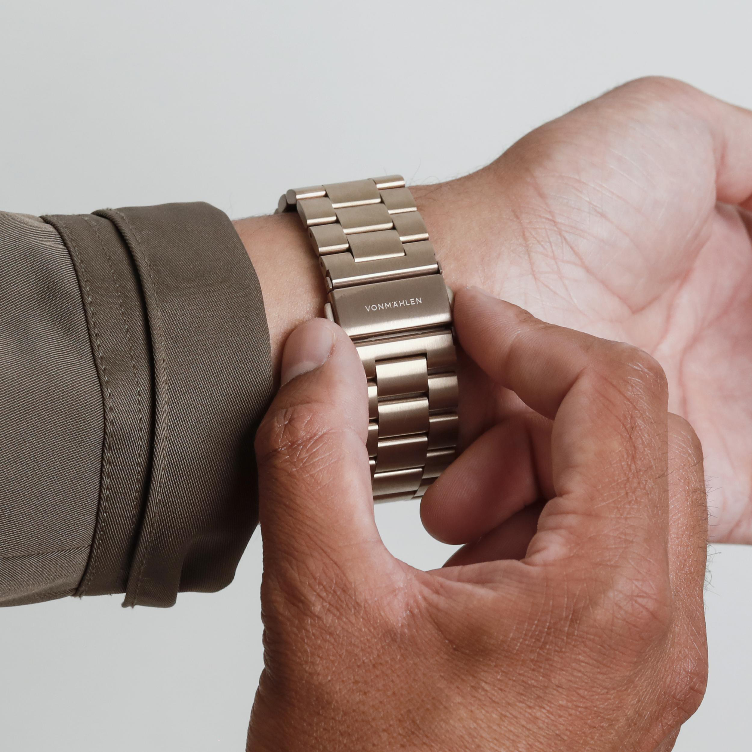 Eine Person mit brauner Kleidung verstellt ein silbernes Armbanduhr-Armband.
