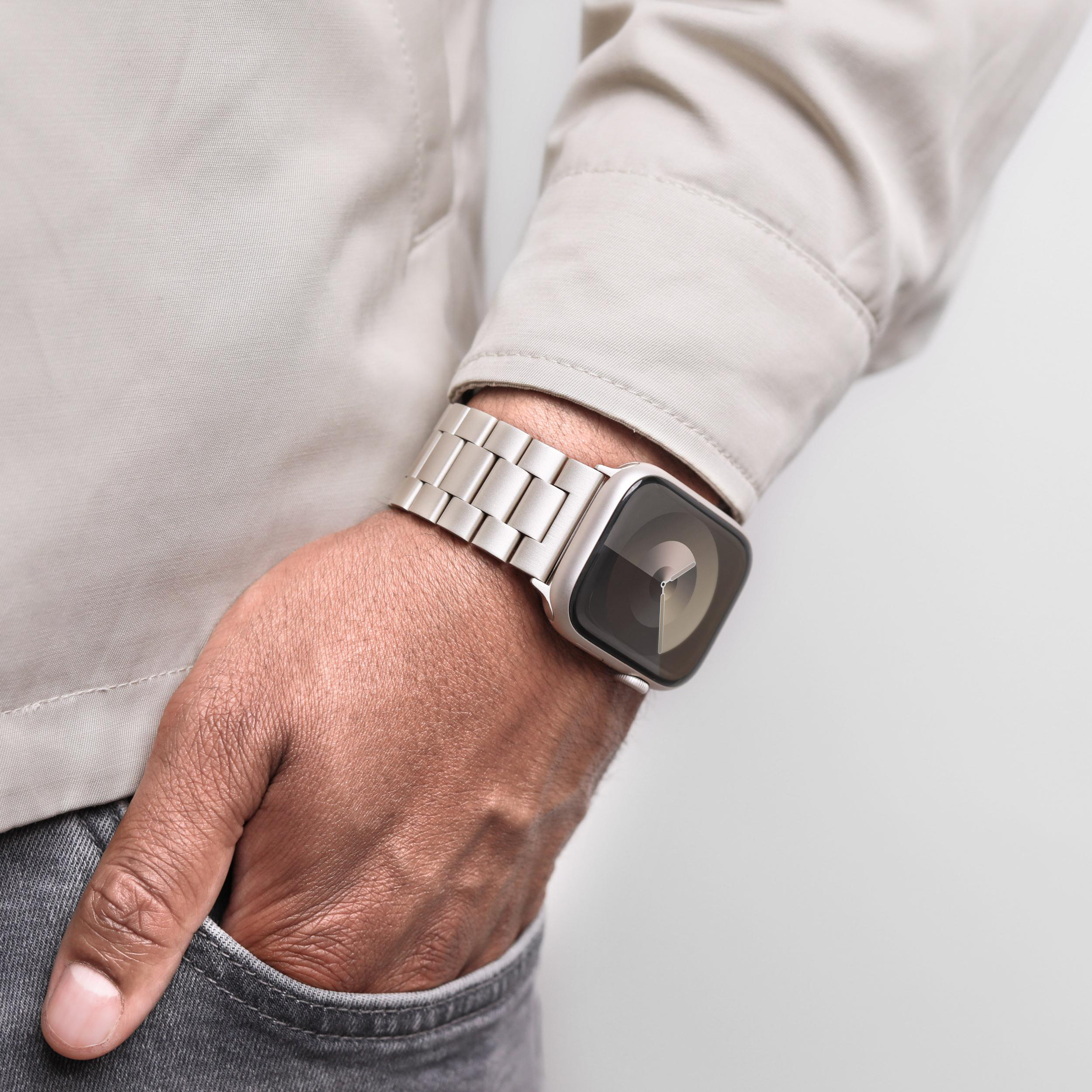 Eine Person trägt eine helle Jacke, graue Jeans und eine Smartwatch am linken Handgelenk.