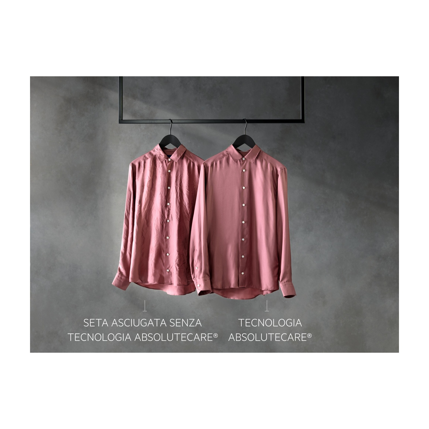Due camicie di seta rosa antico pendono da grucce nere su sfondo grigio.