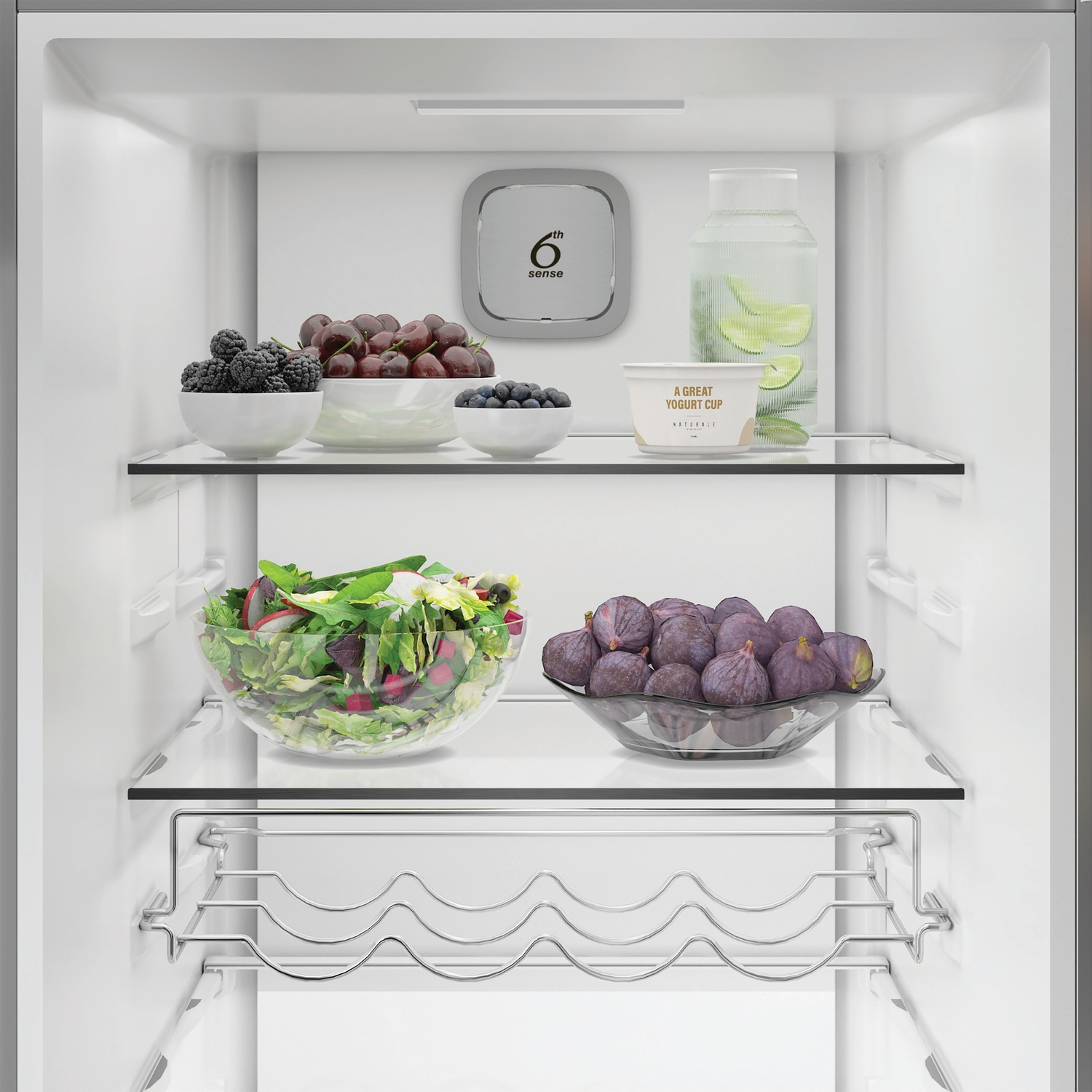 Un réfrigérateur garni de fruits, yaourt et salade sur des étagères en verre.