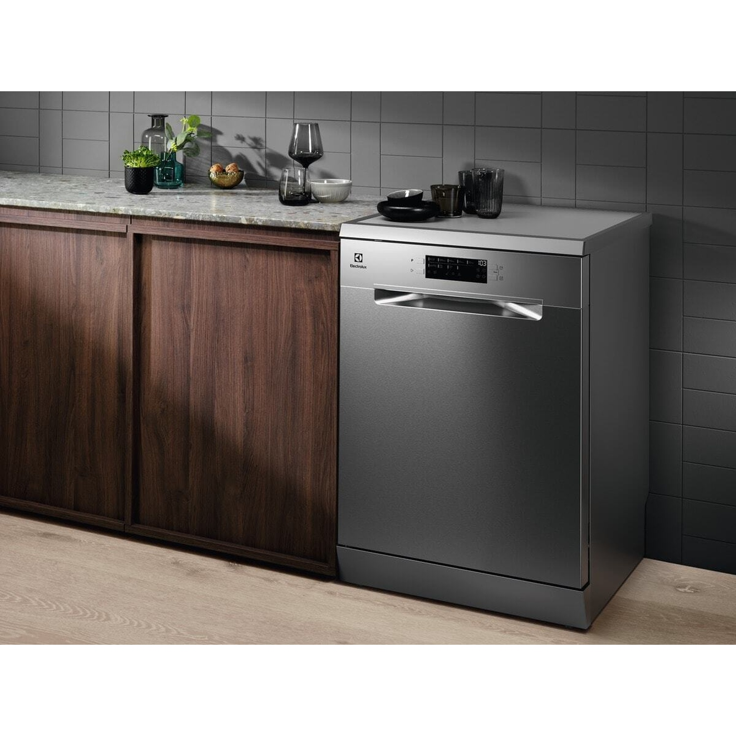 Una lavastoviglie argentata si trova su un pavimento in legno accanto ad armadi in legno scuro in una cucina.