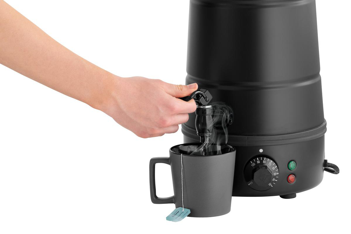 Eine Hand betätigt den Zapfhahn eines schwarzen Wasserkochers, heiße Flüssigkeit fließt in graue Tasse.