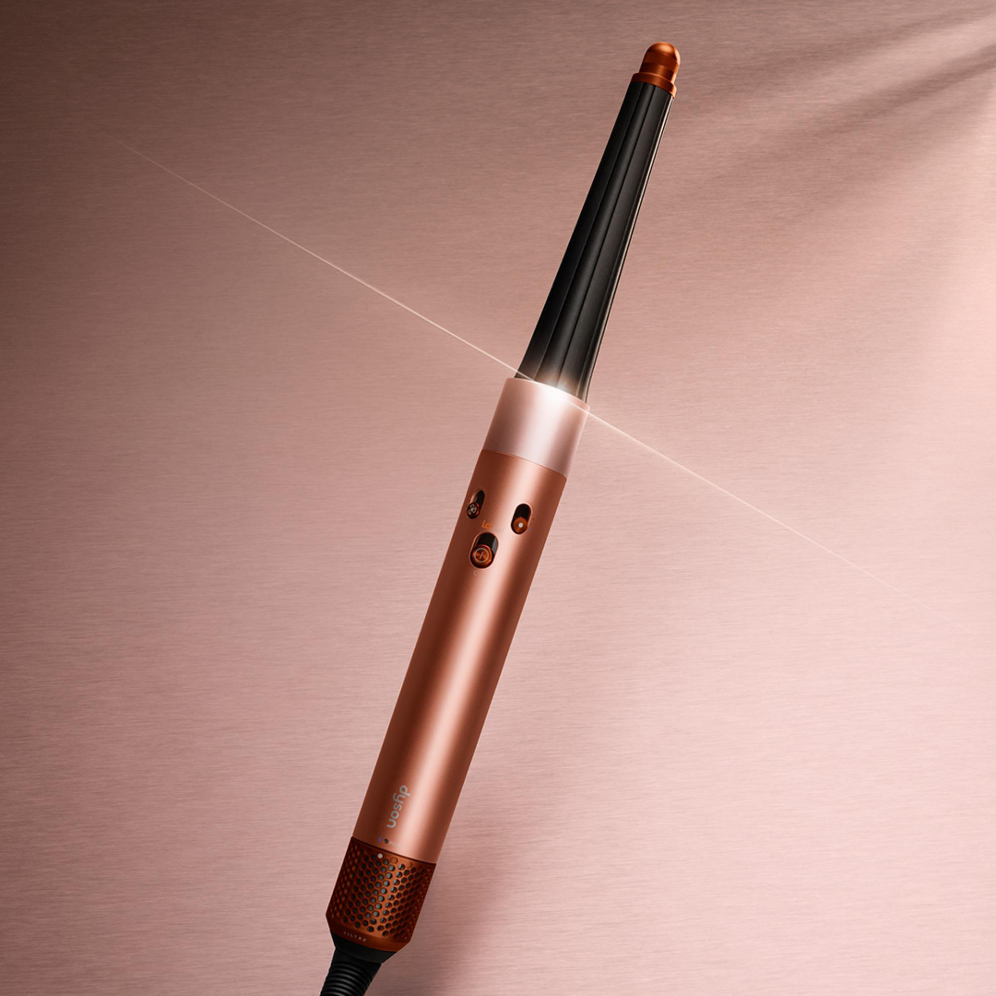 Ein bronzefarbener Haarglätter mit schwarzem Zylinder auf einem roségoldenen Untergrund.