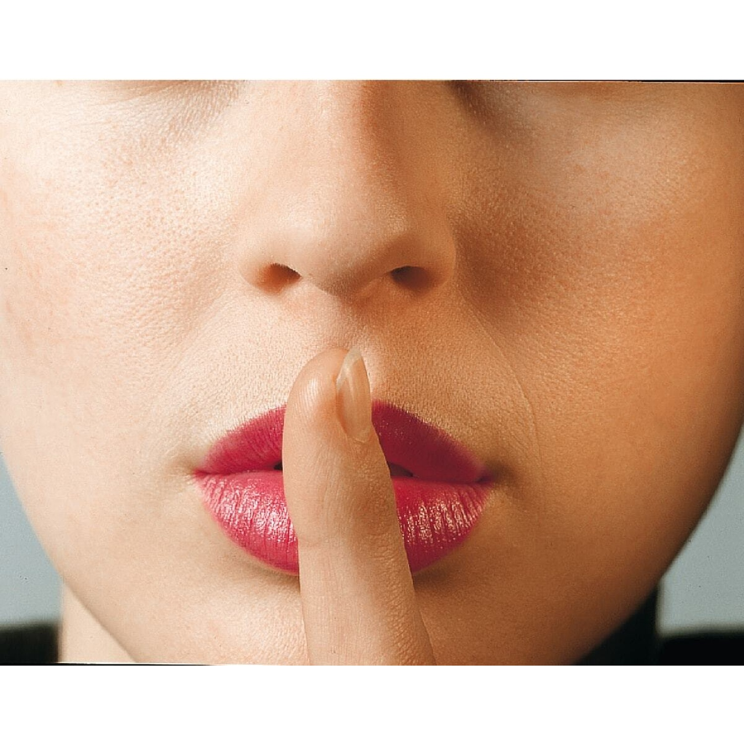 Primo piano delle labbra di una donna con rossetto rosso, che tiene un dito sulla bocca.
