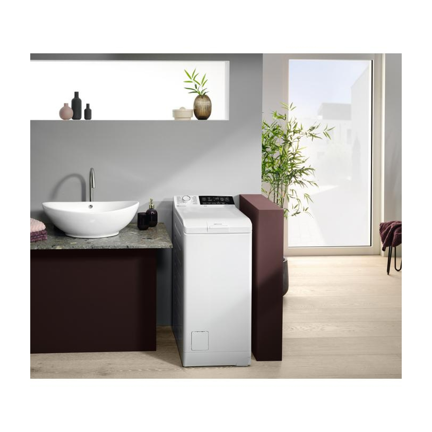 Lavatrice bianca accanto a lavandino e pianta in bagno moderno.