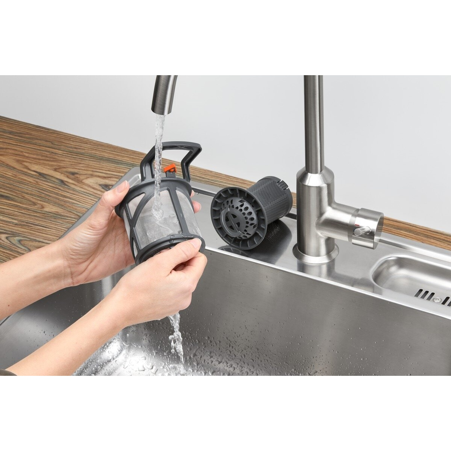 Le mani sciacquano un filtro della lavastoviglie sotto acqua corrente in un lavandino.
