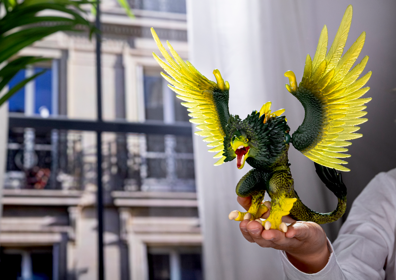 Ein grüner Greif mit gelben Flügeln wird in einer Hand gehalten.