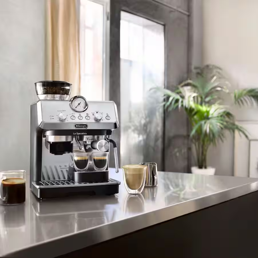 Una cafetera espresso plateada prepara café en dos vasos. Otro vaso de café está al lado.
