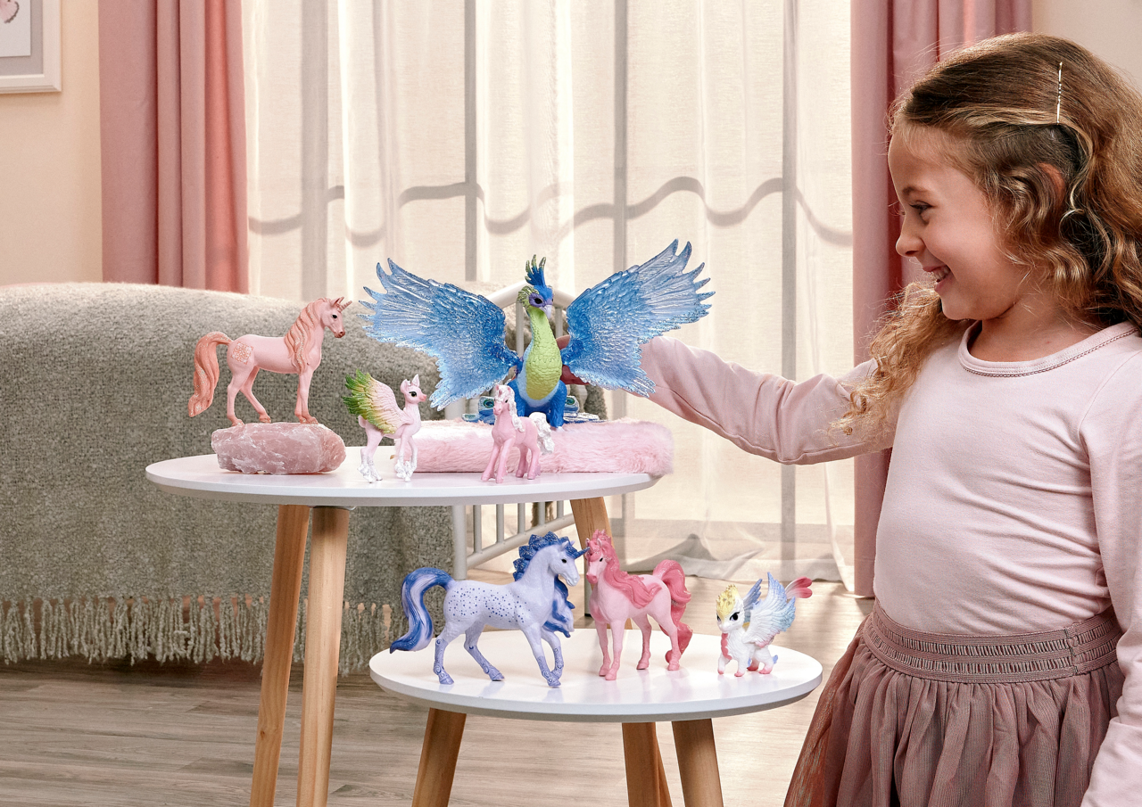 Ein Mädchen spielt mit magischen Tierfiguren, darunter Einhörner und ein Drache.