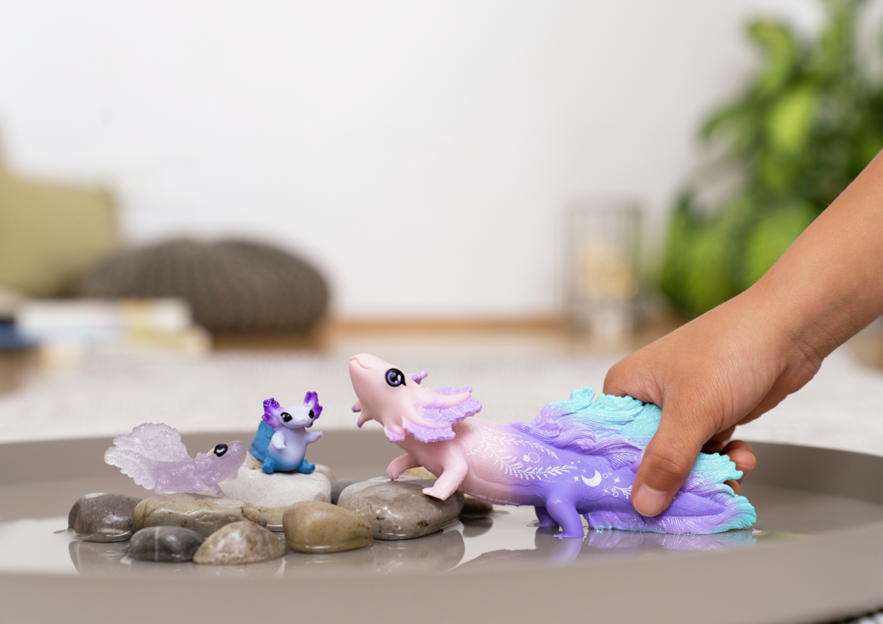 Hand greift nach lila-blauem axolotl-Spielzeug auf Steinen in Wasser.