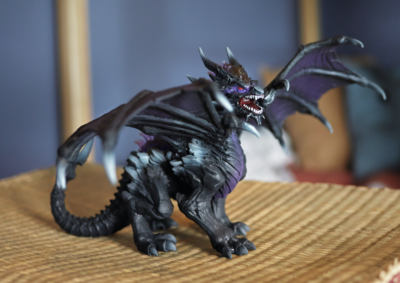 Eine dunkle Drachenfigur mit lila Flügeln auf einer braunen Matte.
