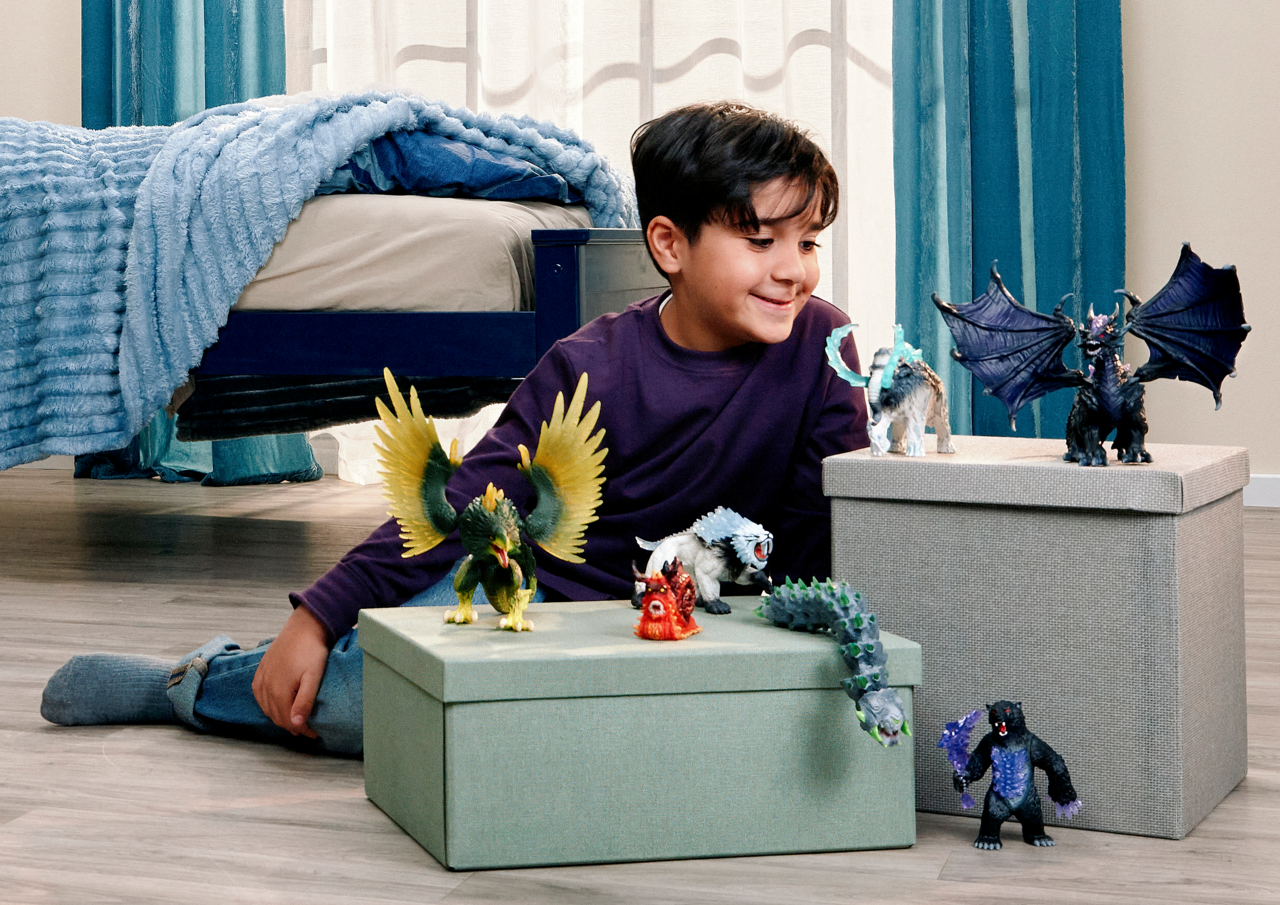 Ein Junge spielt mit Fantasie-Actionfiguren neben einem Bett und Spielzeugkisten.