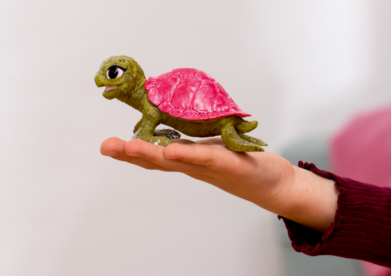 Grüne Spielzeugschildkröte mit rosa Panzer auf einer Hand.