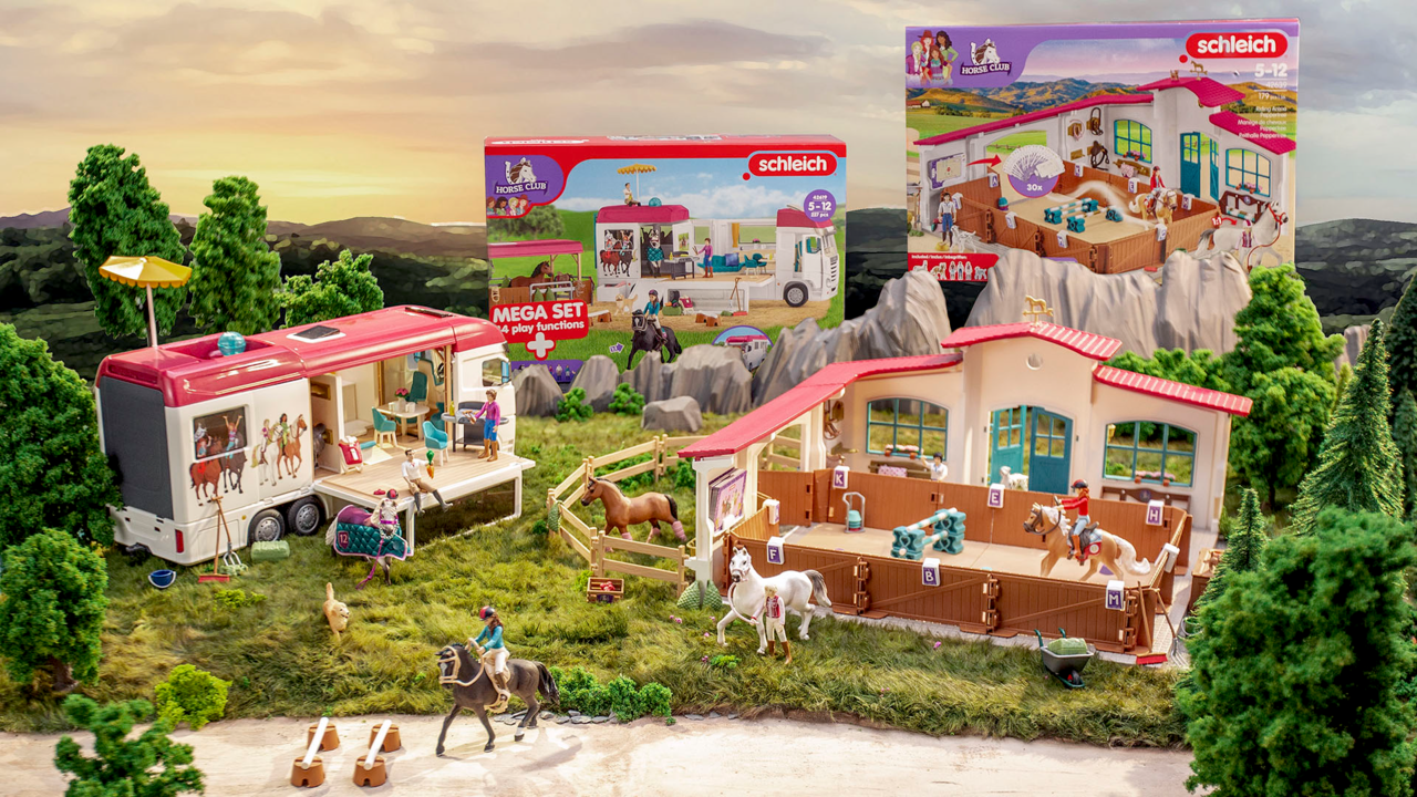 Spielzeug-Reiterhof mit Pferdetransporter, Stall und Figuren vor einer Bergkulisse.
